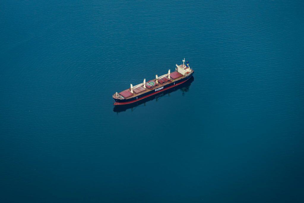 An aerial view of a cargo ship navigating calm blue waters, representing the essential role of ocean shipping in global trade and logistics.